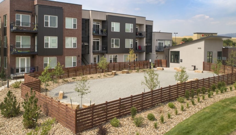 Cycle Apartments Fort Collins offers modern three-story buildings with balconies, a fenced gravel courtyard featuring young trees and rocks, and elegant landscaping with shrubs and stones surrounding the peaceful outdoor space.
