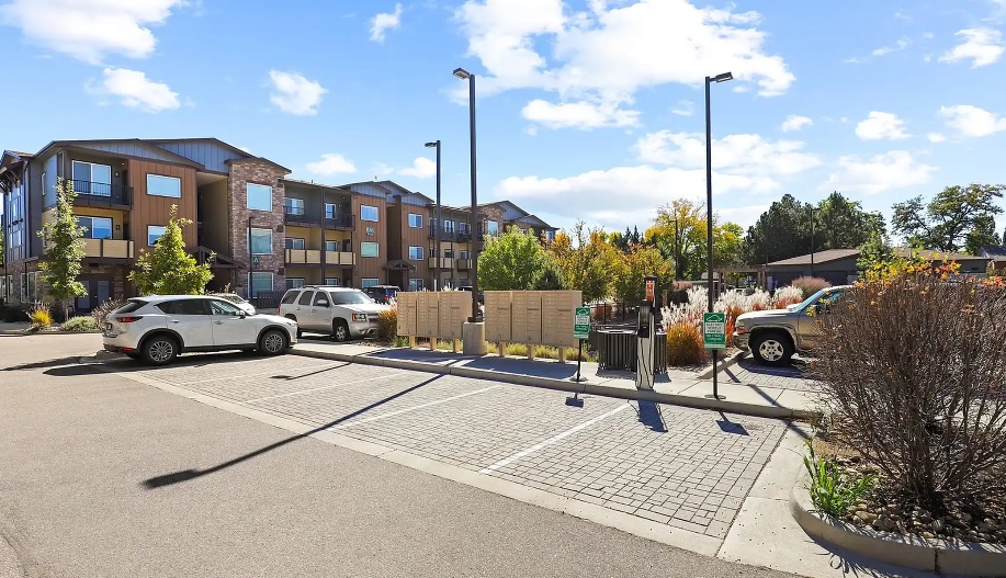 Copperleaf Place Fort Collins features modern apartment buildings, several parked cars, a cluster of mailboxes, and landscaped greenery under a partly cloudy sky.