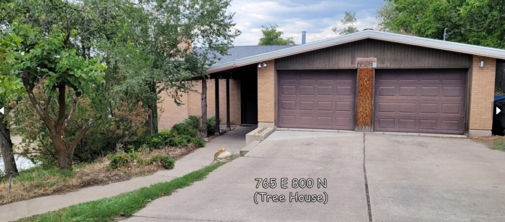 A brick house with a wooden two-car garage and sloped driveway, surrounded by trees and greenery in Auburn Heights. The address 766 E 800 N (Auburn Heights Tree House Logan) is overlaid on the photo.