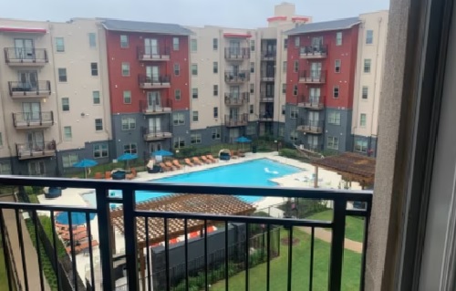 Enjoy a stunning view from your balcony at 848 Mitchell Arlington, overlooking a large outdoor swimming pool with lounge chairs, surrounded by a multi-story apartment complex with striking red and gray exterior walls.